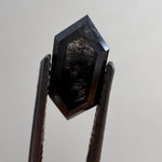 Close-up of a 1.36ct natural black elongated hexagon step cut diamond held in tweezers, showcasing its striking dark geometric facets. GIA certified and sourced for MOHSTEN bespoke custom engagement rings in Auckland, New Zealand.