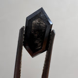 Close-up of a 1.36ct natural black elongated hexagon step cut diamond held in tweezers, showcasing its striking dark geometric facets. GIA certified and sourced for MOHSTEN bespoke custom engagement rings in Auckland, New Zealand.