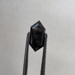 Close-up of a 1.36ct natural black elongated hexagon step cut diamond held in tweezers, showcasing its striking dark geometric facets. GIA certified and sourced for MOHSTEN bespoke custom engagement rings in Auckland, New Zealand.