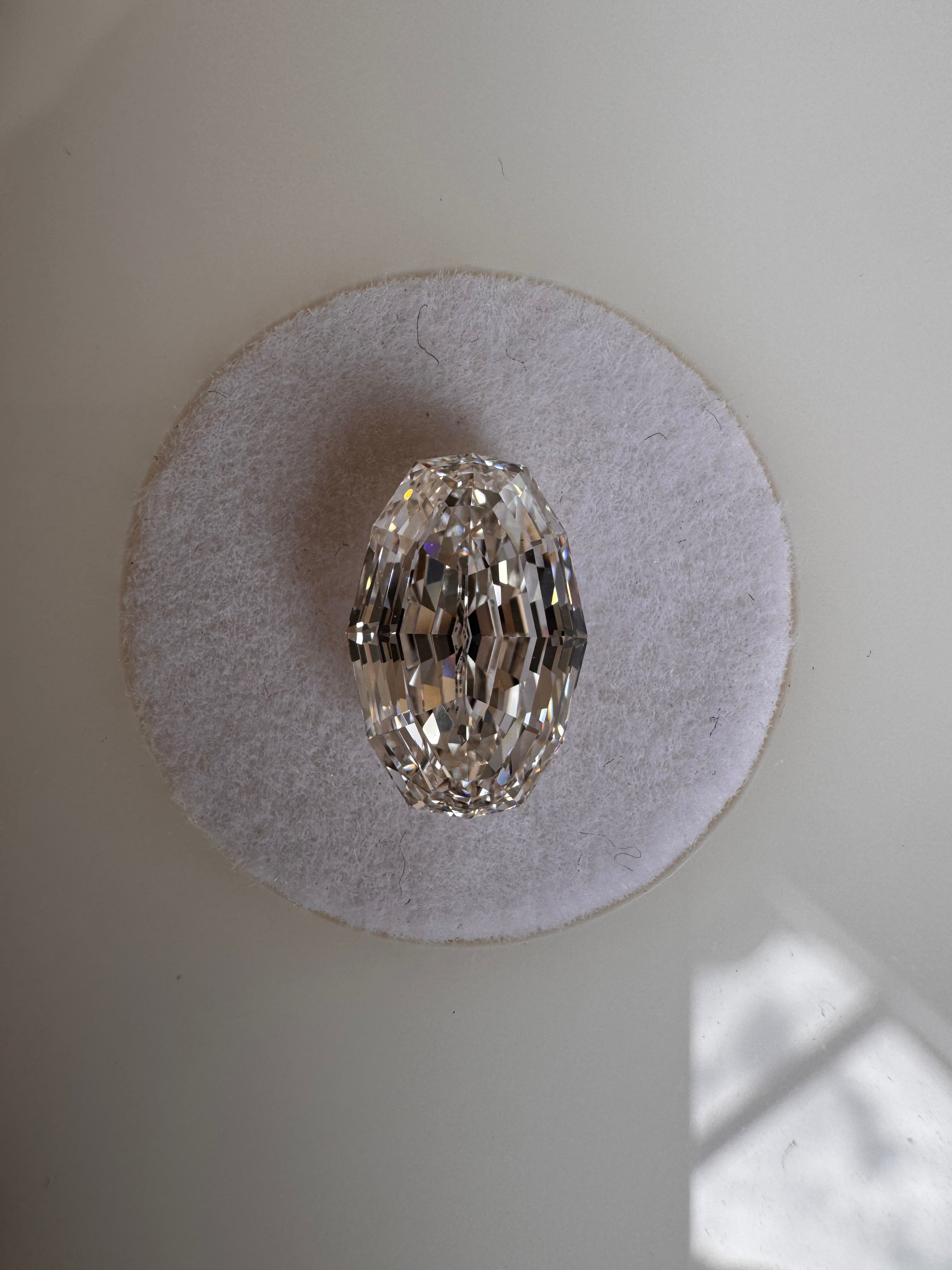 A loose 2.09ct oval step cut lab-grown diamond resting flat on a round white felt pad. Sourced for bespoke custom engagement rings by MOHSTEN jewellery studio in Auckland, New Zealand.