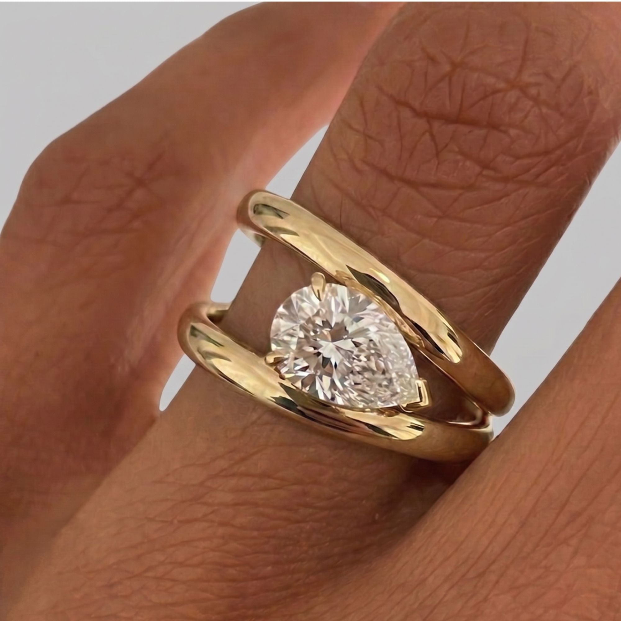 Gold ring with a pear diamond on a finger against a neutral background
