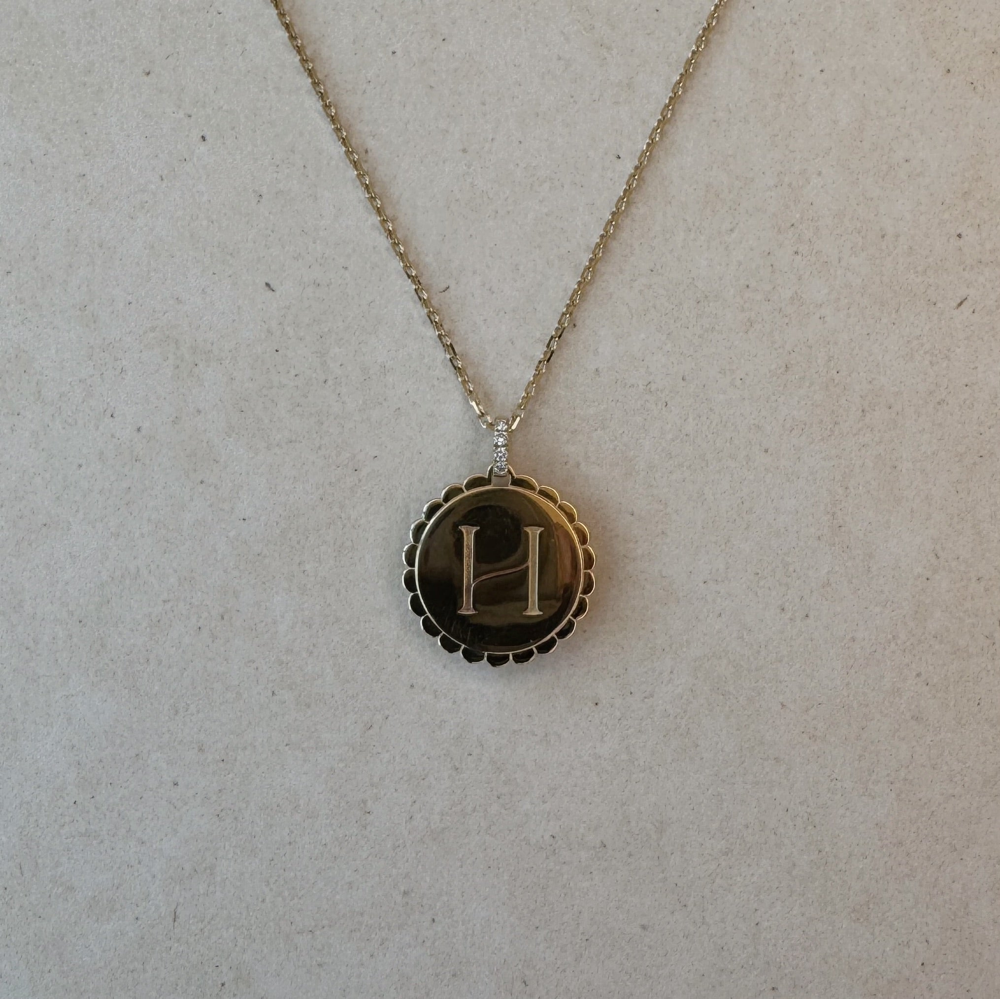 Reversible 9ct gold ‘H’ pendant with scalloped edge and diamond rotating bail, engraved on one side and polished on the reverse.