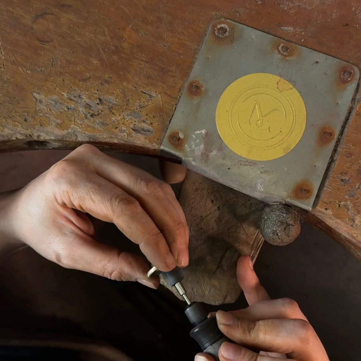Close-up of hands working with a tool on a metal surface with a yellow circular mark.
