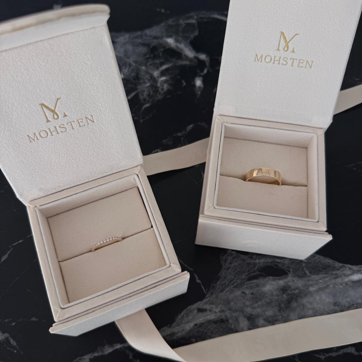Jewelry box with gold ring inside on a dark marble surface, featuring the brand 'MOHSTEN'.