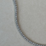 Close-up of a diamond tennis necklace on a light gray background