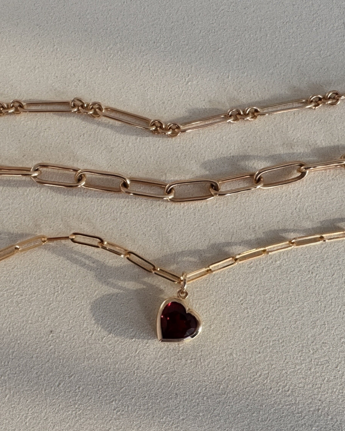 MOHSTEN A  gold layered necklace image featuring a paperclip chain, a paperclip chain with a small heart-shaped pendant, and a delicate paperclip chain.