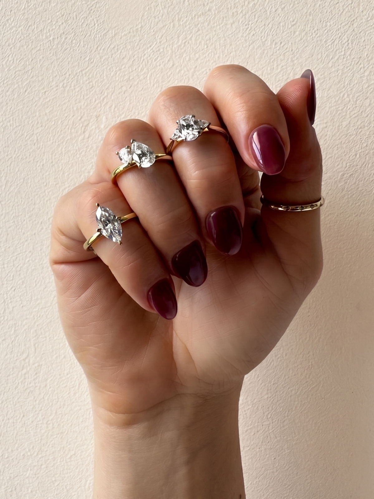 Hand wearing multiple diamond rings on a beige background