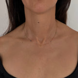 MOHSTEN mini personalised 9ct gold charm necklace featuring custom initials and birthstones, modeled on a woman's neck.