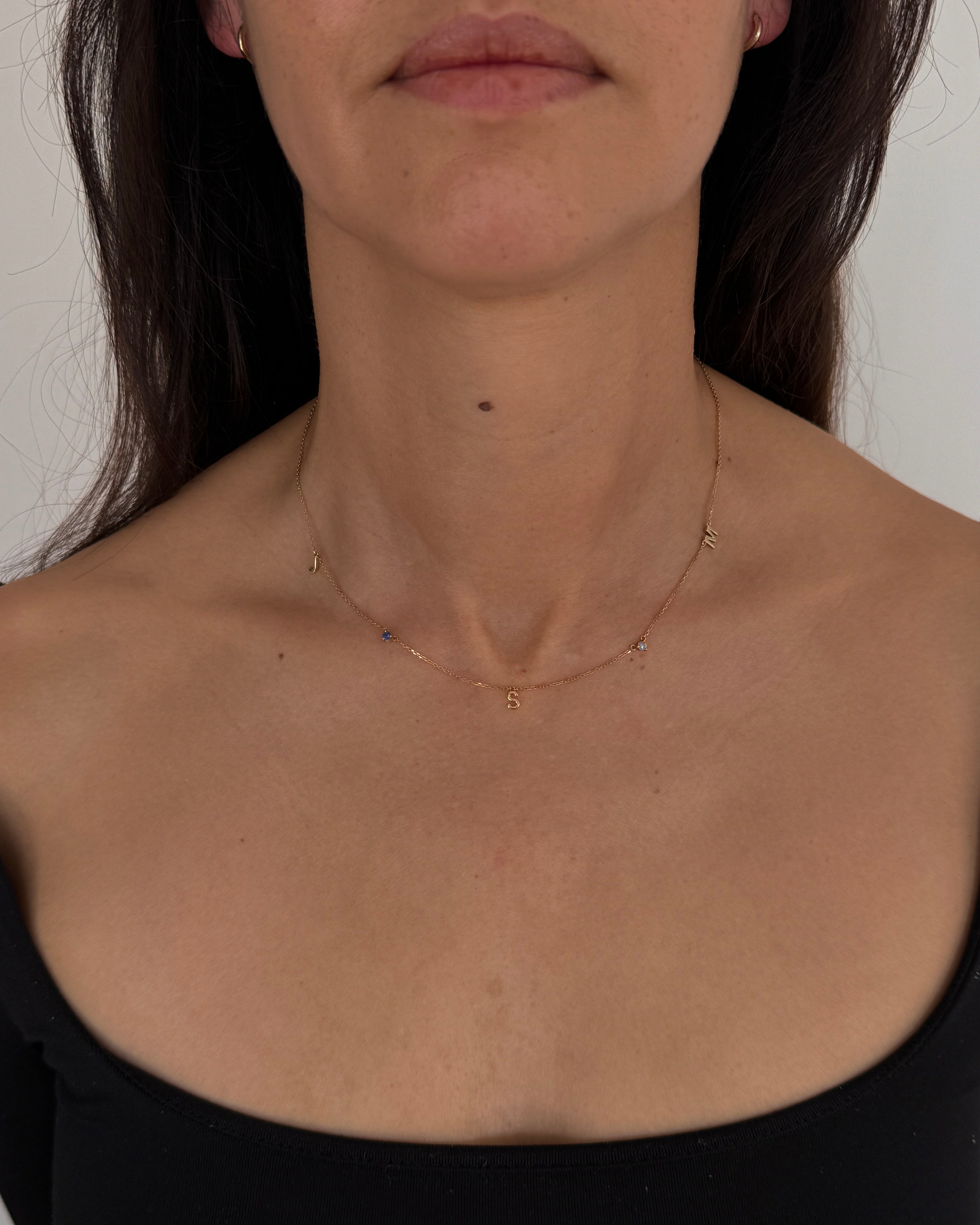 MOHSTEN mini personalised 9ct gold charm necklace featuring custom initials and birthstones, modeled on a woman's neck.