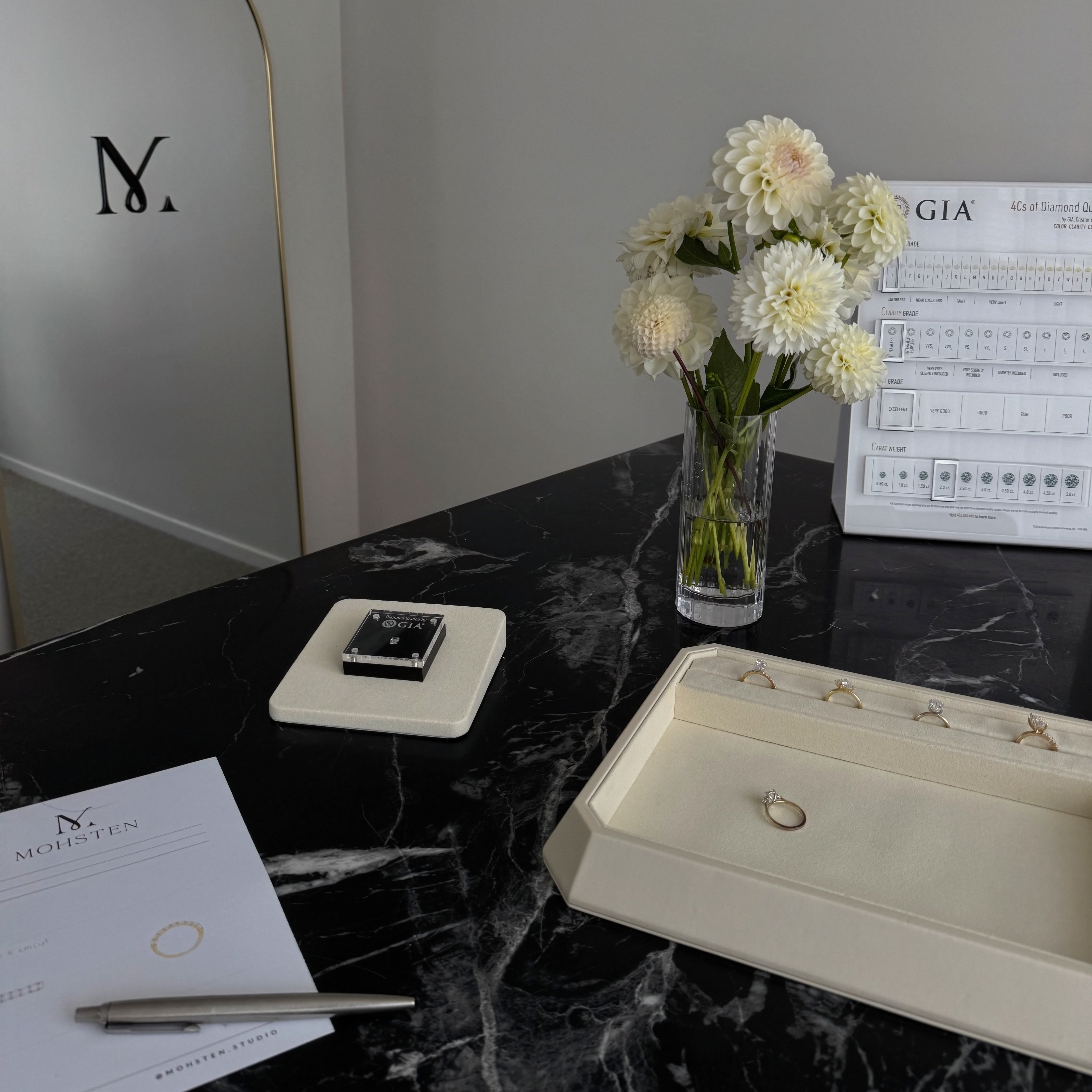 Jewelry box with rings, a vase of flowers, and a GIA document on a marble surface.