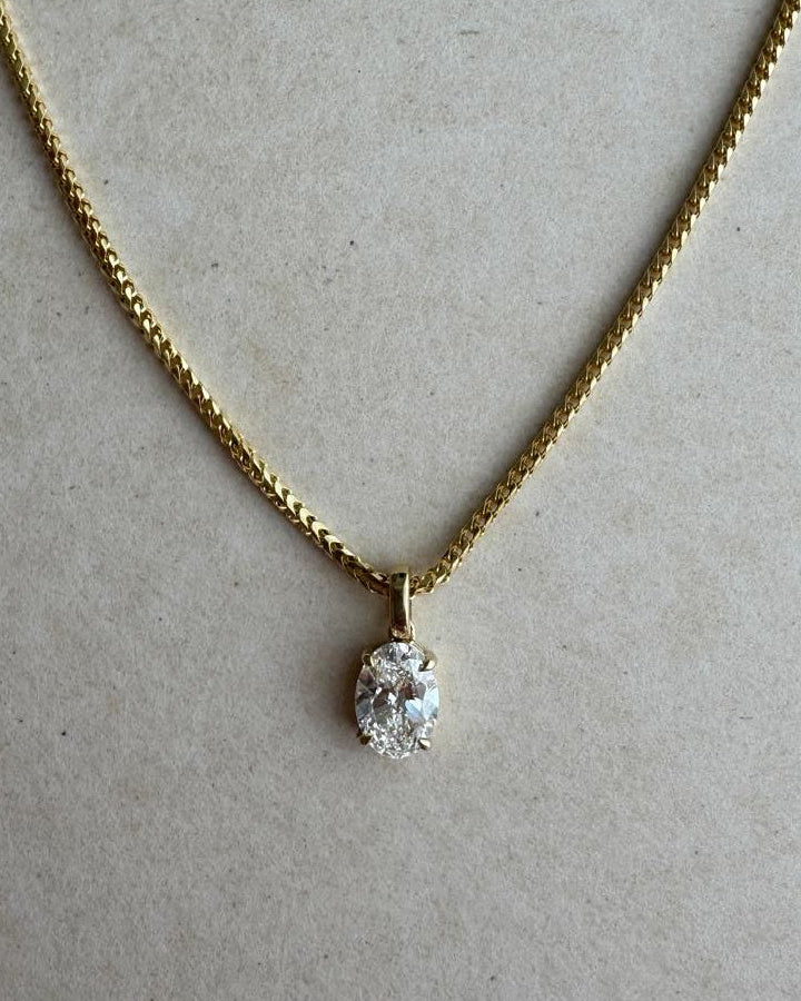 Gold necklace with a diamond pendant on a beige background