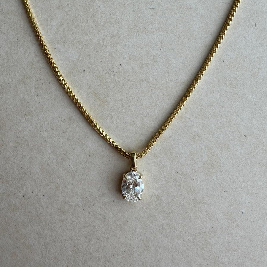 Gold necklace with a diamond pendant on a beige background