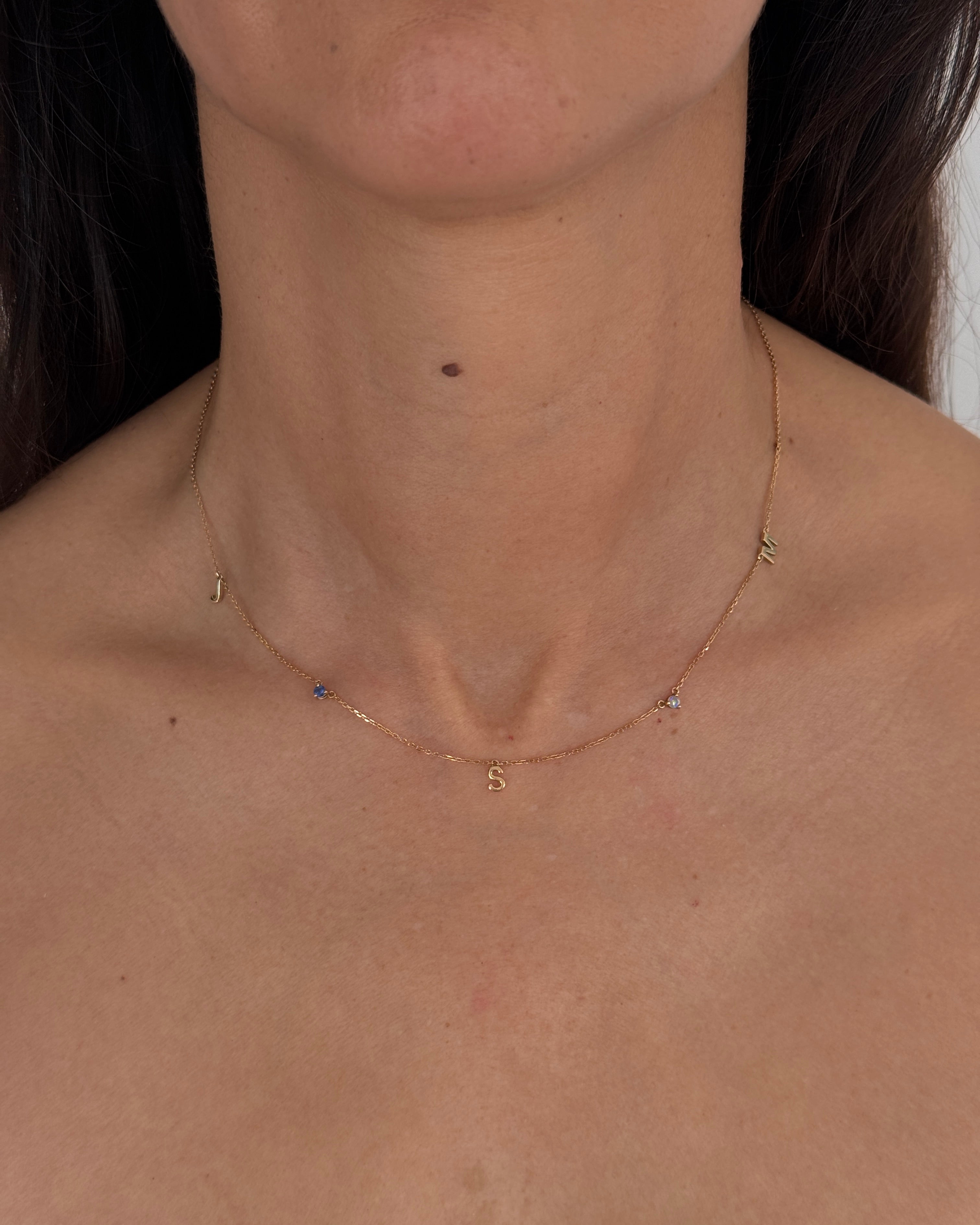 MOHSTEN personalised 9ct gold charm necklace with custom initials and blue birthstones, modeled on the neck.