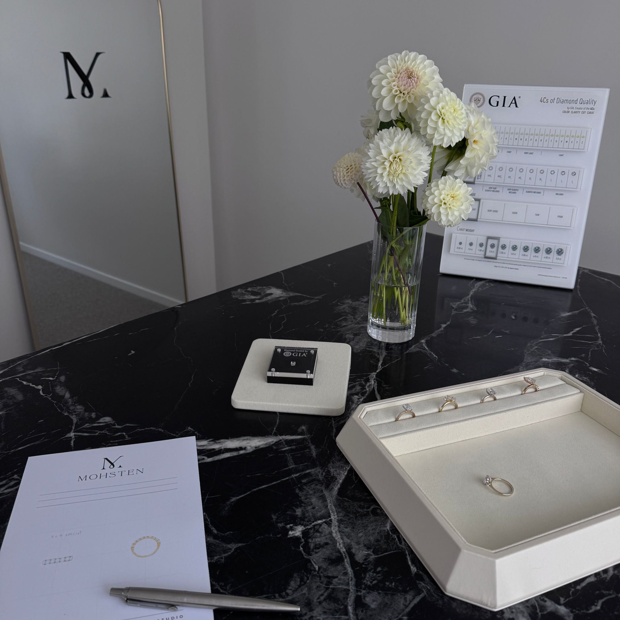 Jewelry display with rings, a vase of flowers, and GIA certificate on a black marble surface.