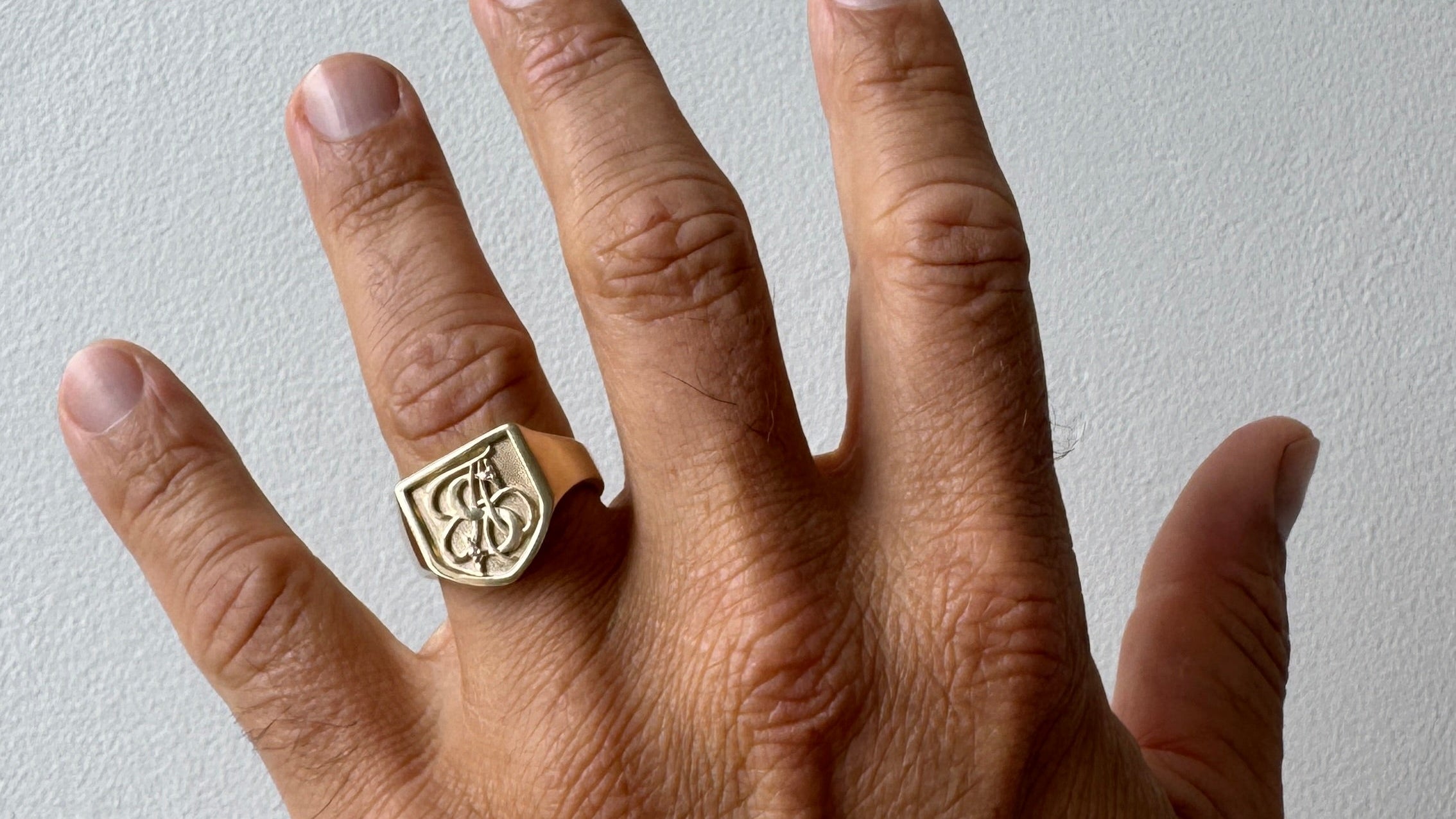 Hand wearing a gold ring with a design on a plain background