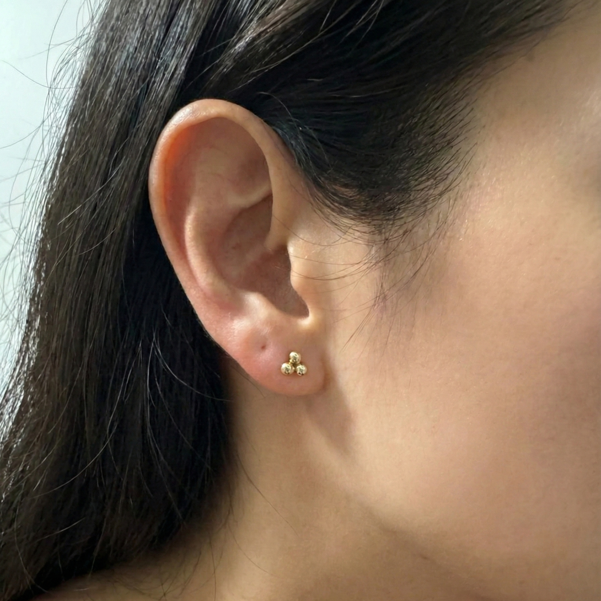 Close-up of an ear wearing a small gold earring with green stones.