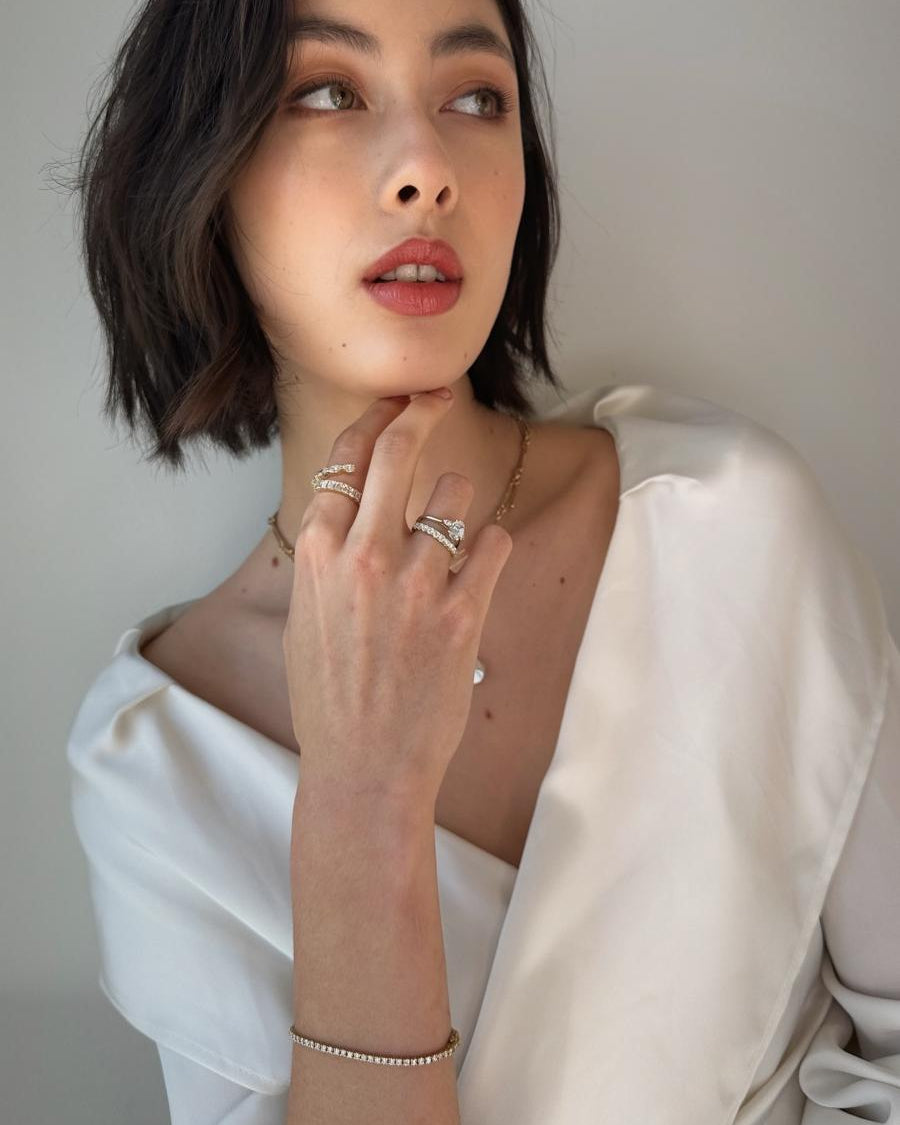 Woman wearing a white top with jewelry against a neutral background