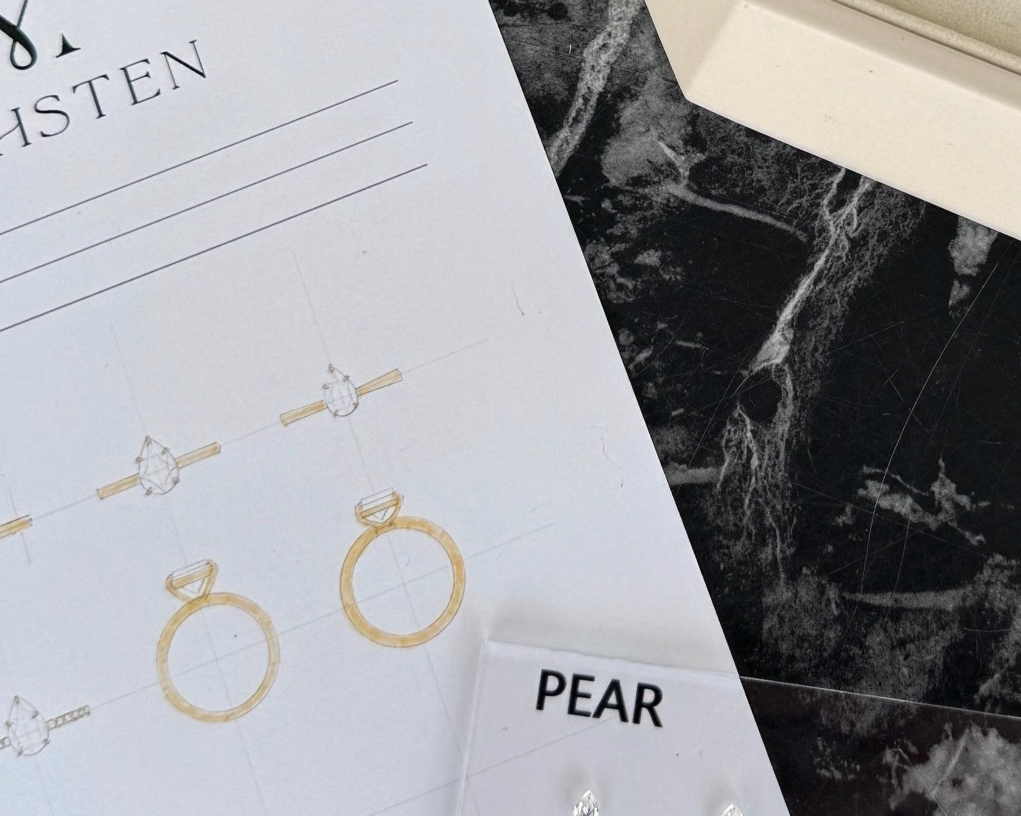 Jewellery display with rings in a box on a marble surface, featuring the brand 'Mohsten'.