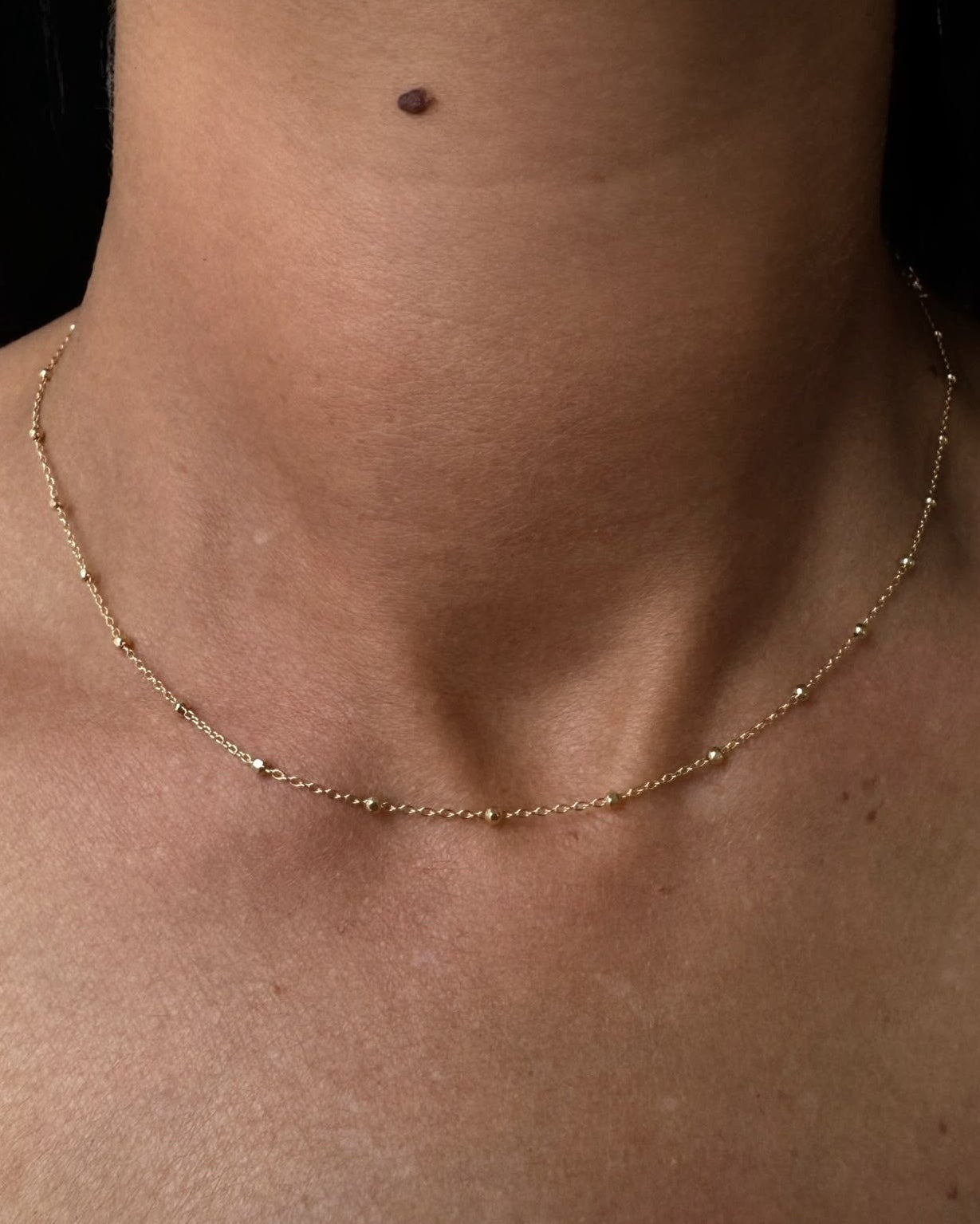 Close-up of a person's neck with a gold necklace against a dark background
