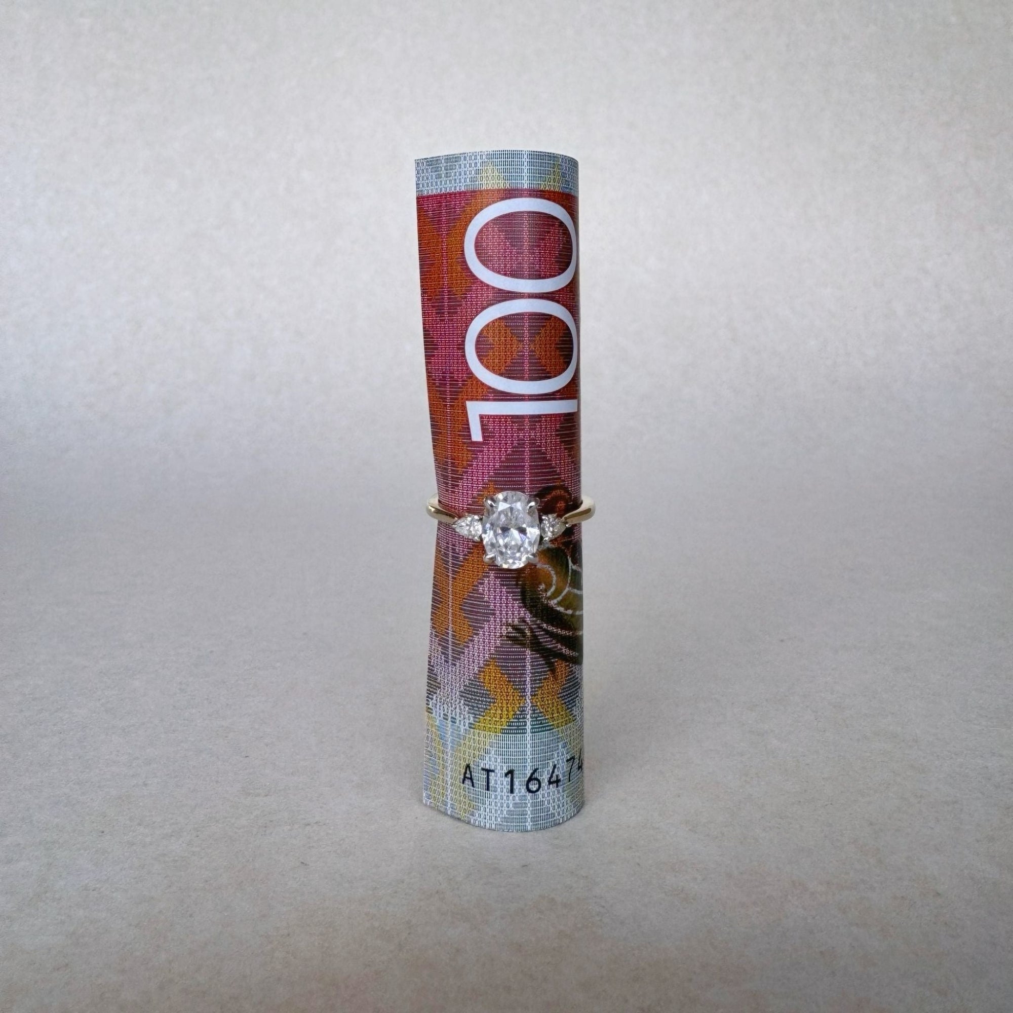 Engagement ring on a cylindrical object with '100' printed on it against a plain background