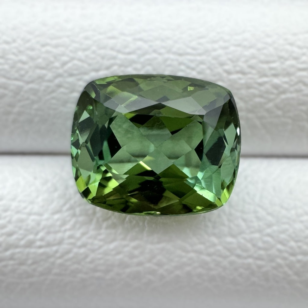 A cushion-cut green gemstone with faceted edges loose