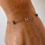 Gold bracelet with a letter 'H' charm on a wrist against a white background