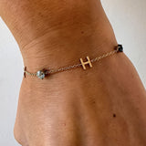 Gold bracelet with a letter 'H' charm on a wrist against a white background