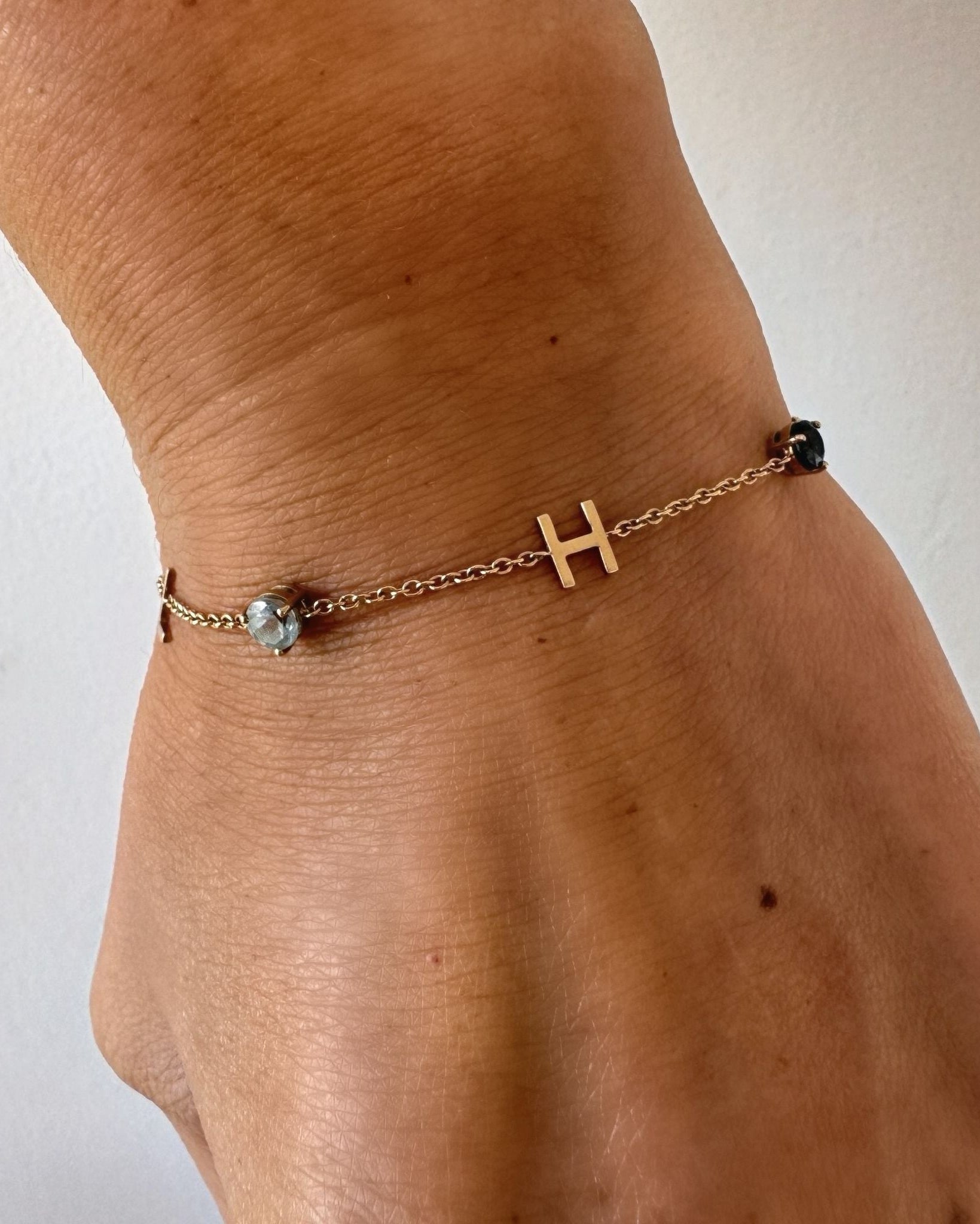 Gold bracelet with a letter 'H' charm on a wrist against a white background