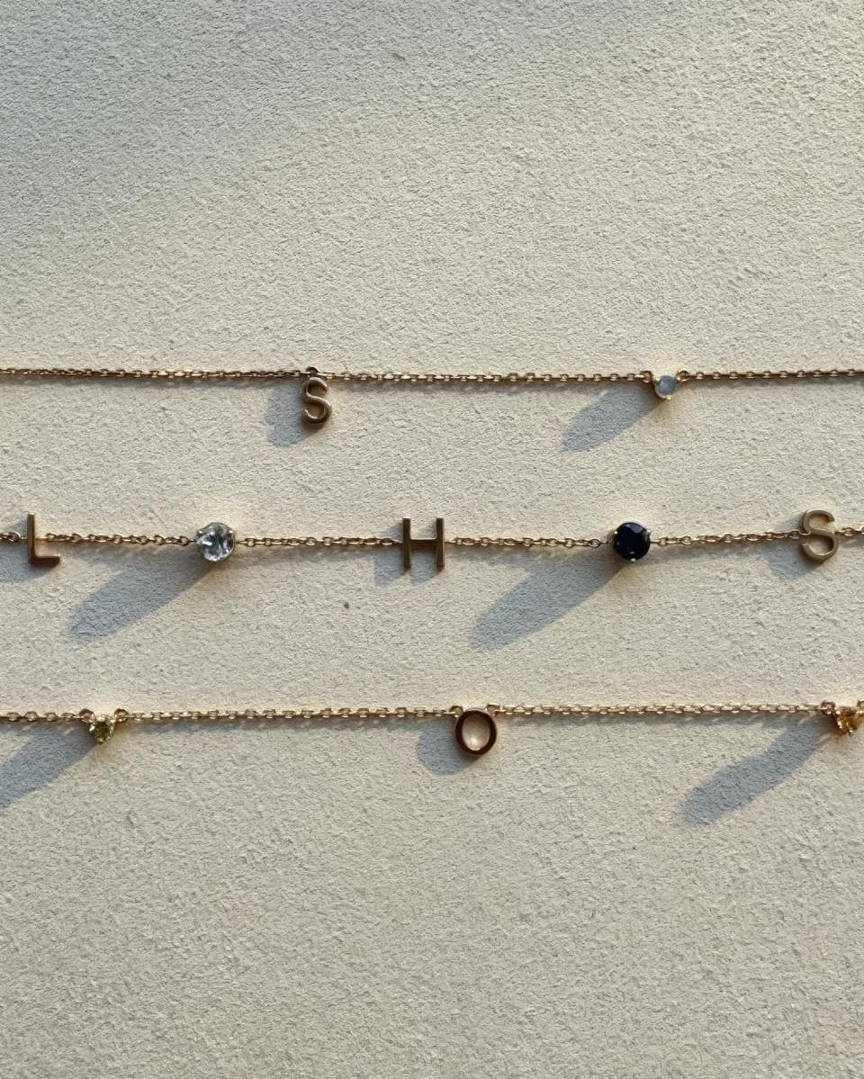 Three gold necklaces with letter charms on a light gray background