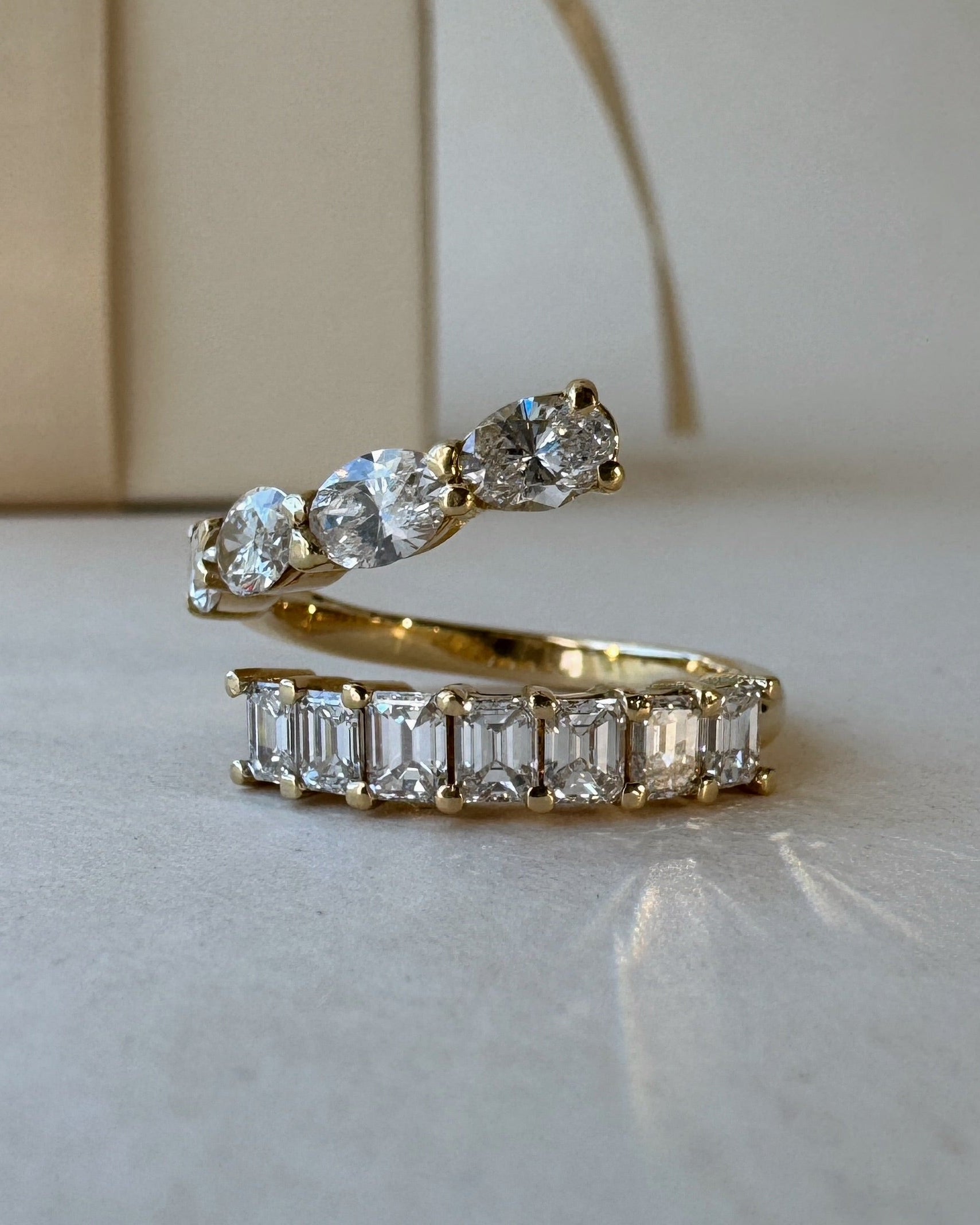 The Azores Wrap ring in yellow gold resting on a smooth surface, highlighting the brilliance of its 2.00ctw emerald and oval cut lab-grown diamonds.