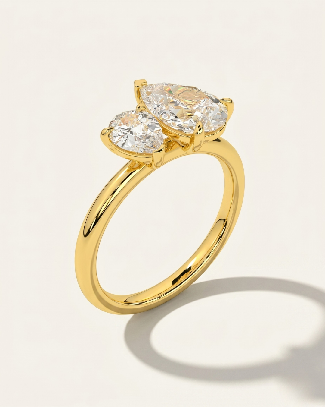 MOHSTEN Cairo pear diamond Toi et Moi engagement ring in 18ct yellow gold showcasing a three-quarter perspective view of the two asymmetrical pear-cut diamonds casting a prominent architectural shadow on a light studio background.