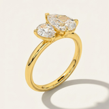 MOHSTEN Cairo pear diamond Toi et Moi engagement ring in 18ct yellow gold showcasing a three-quarter perspective view of the two asymmetrical pear-cut diamonds casting a prominent architectural shadow on a light studio background.