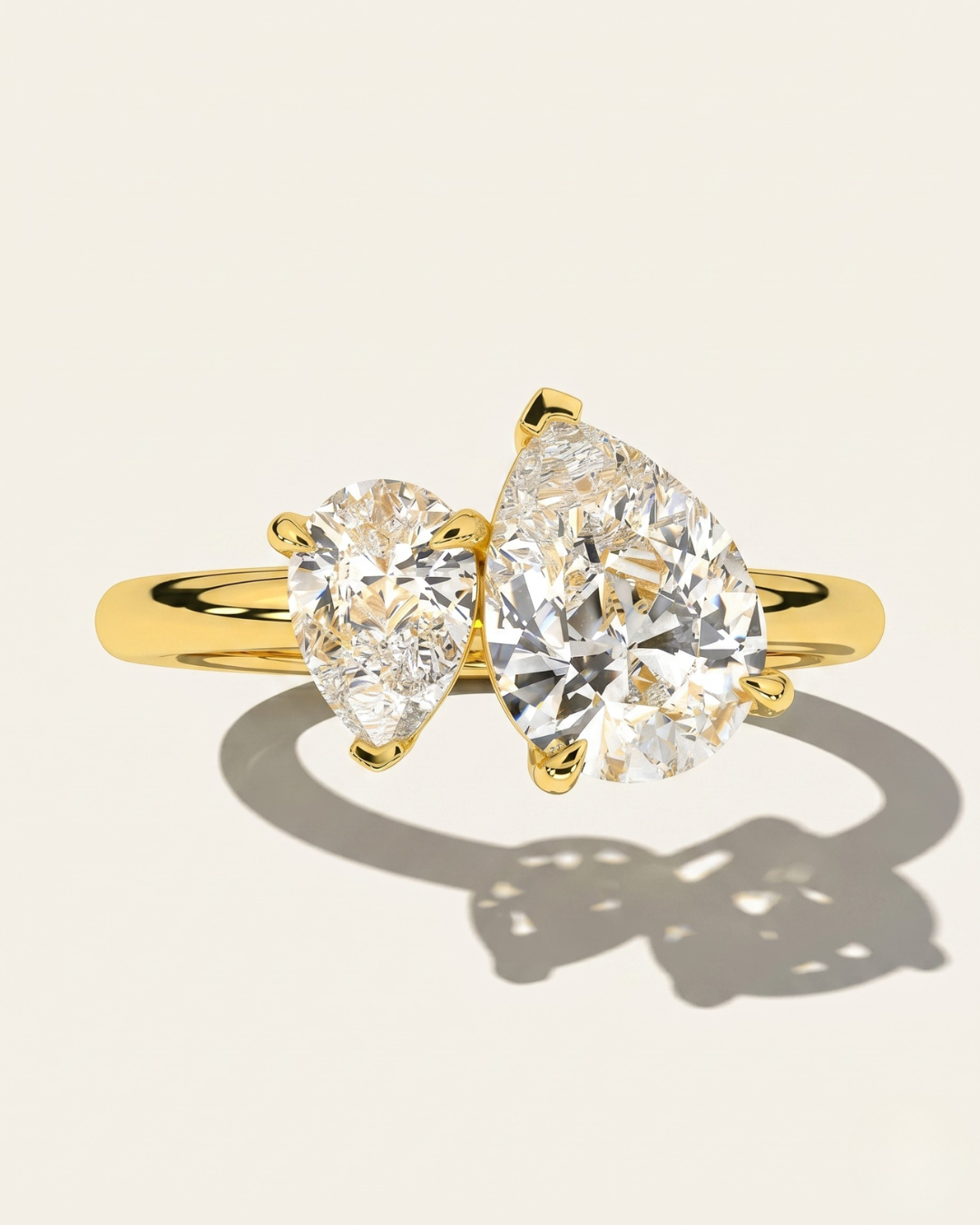 MOHSTEN Cairo pear diamond Toi et Moi engagement ring in 18ct yellow gold showcasing a macro face-on view of the two asymmetrical pear-cut diamonds casting a sharp architectural shadow on a warm studio background.