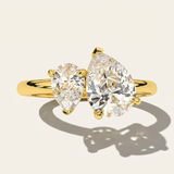 MOHSTEN Cairo pear diamond Toi et Moi engagement ring in 18ct yellow gold showcasing a macro face-on view of the two asymmetrical pear-cut diamonds casting a sharp architectural shadow on a warm studio background.