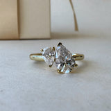 MOHSTEN Cairo pear diamond Toi et Moi engagement ring in 18ct yellow gold in a close-up studio perspective view, highlighting the asymmetrical pairing of the two pear-cut diamonds against a minimalist warm background.
