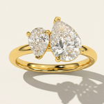 MOHSTEN Cairo pear diamond Toi et Moi engagement ring in 18ct yellow gold, showcasing a crisp macro top view of the two asymmetrical pear-cut diamonds and their distinct architectural shadow on a warm studio background.