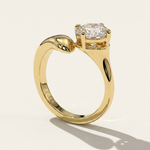 Side profile view of the MOHSTEN Granada asymmetric round diamond solitaire engagement ring in 18ct yellow gold, showcasing the unique low-profile basket setting and sweeping band architecture casting a distinct shadow on a warm studio background.