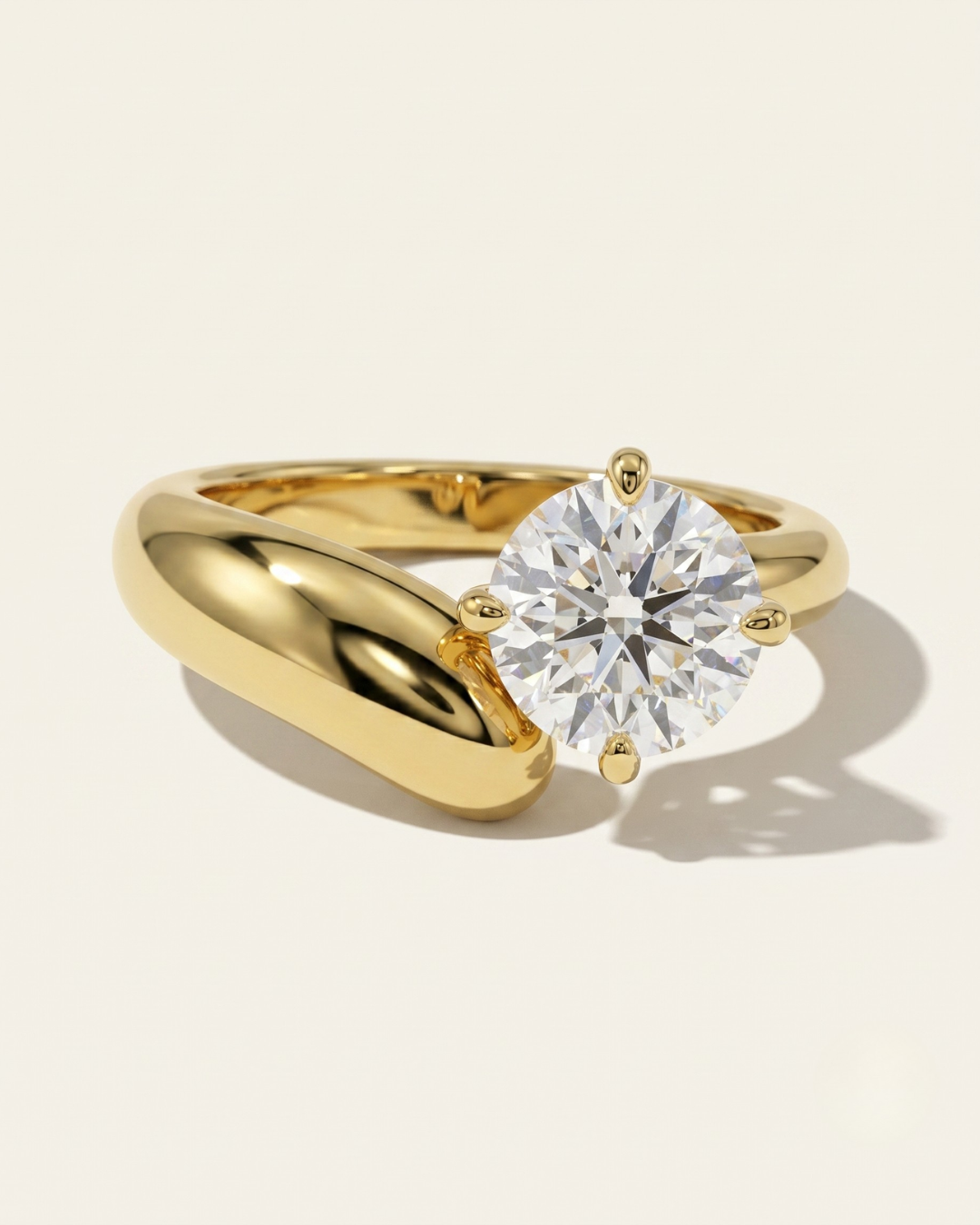 MOHSTEN Granada asymmetric round diamond solitaire engagement ring in 18ct yellow gold showcasing an offset round brilliant diamond on a bold, organic sweeping band casting a soft shadow on a warm studio background.