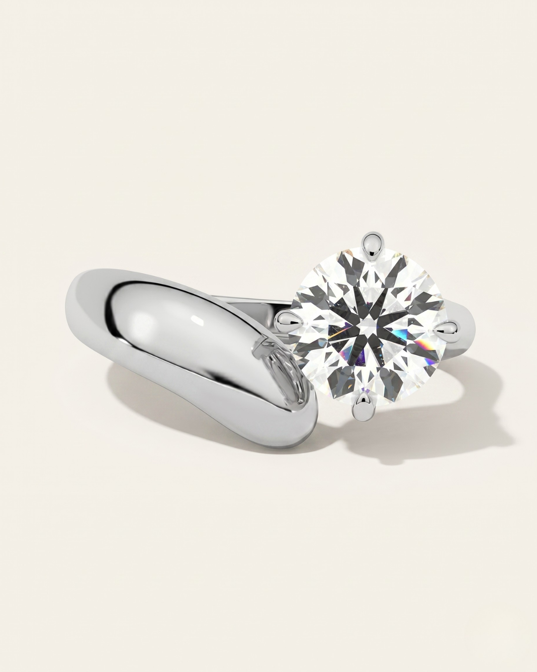MOHSTEN Granada asymmetric round diamond solitaire engagement ring in polished platinum showcasing a face-on studio view of the offset round brilliant centre diamond on a bold, sculptural wide-swept band casting a soft shadow.