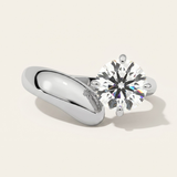 MOHSTEN Granada asymmetric round diamond solitaire engagement ring in polished platinum showcasing a face-on studio view of the offset round brilliant centre diamond on a bold, sculptural wide-swept band casting a soft shadow.