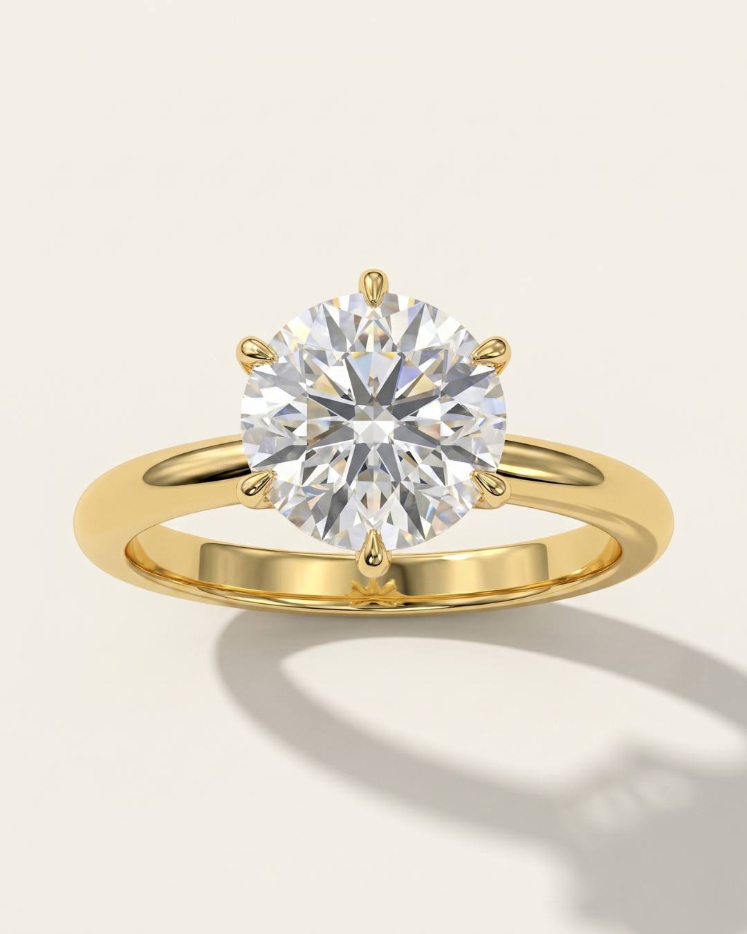 MOHSTEN Jaipur round diamond solitaire engagement ring in 18ct yellow gold displaying a striking face-on view of the round brilliant diamond setting casting an elegant architectural shadow on a minimalist warm studio background.