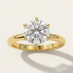 MOHSTEN Jaipur round diamond solitaire engagement ring in 18ct yellow gold displaying a striking face-on view of the round brilliant diamond setting casting an elegant architectural shadow on a minimalist warm studio background.