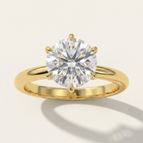 MOHSTEN Jaipur round diamond solitaire engagement ring in 18ct yellow gold displaying a striking face-on view of the round brilliant diamond setting casting an elegant architectural shadow on a minimalist warm studio background.