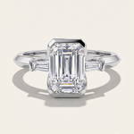 MOHSTEN Montreux 18ct white gold three-stone engagement ring with emerald cut diamond and tapered baguettes.