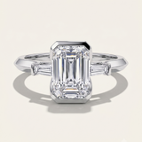 MOHSTEN Montreux 18ct white gold three-stone engagement ring with emerald cut diamond and tapered baguettes.