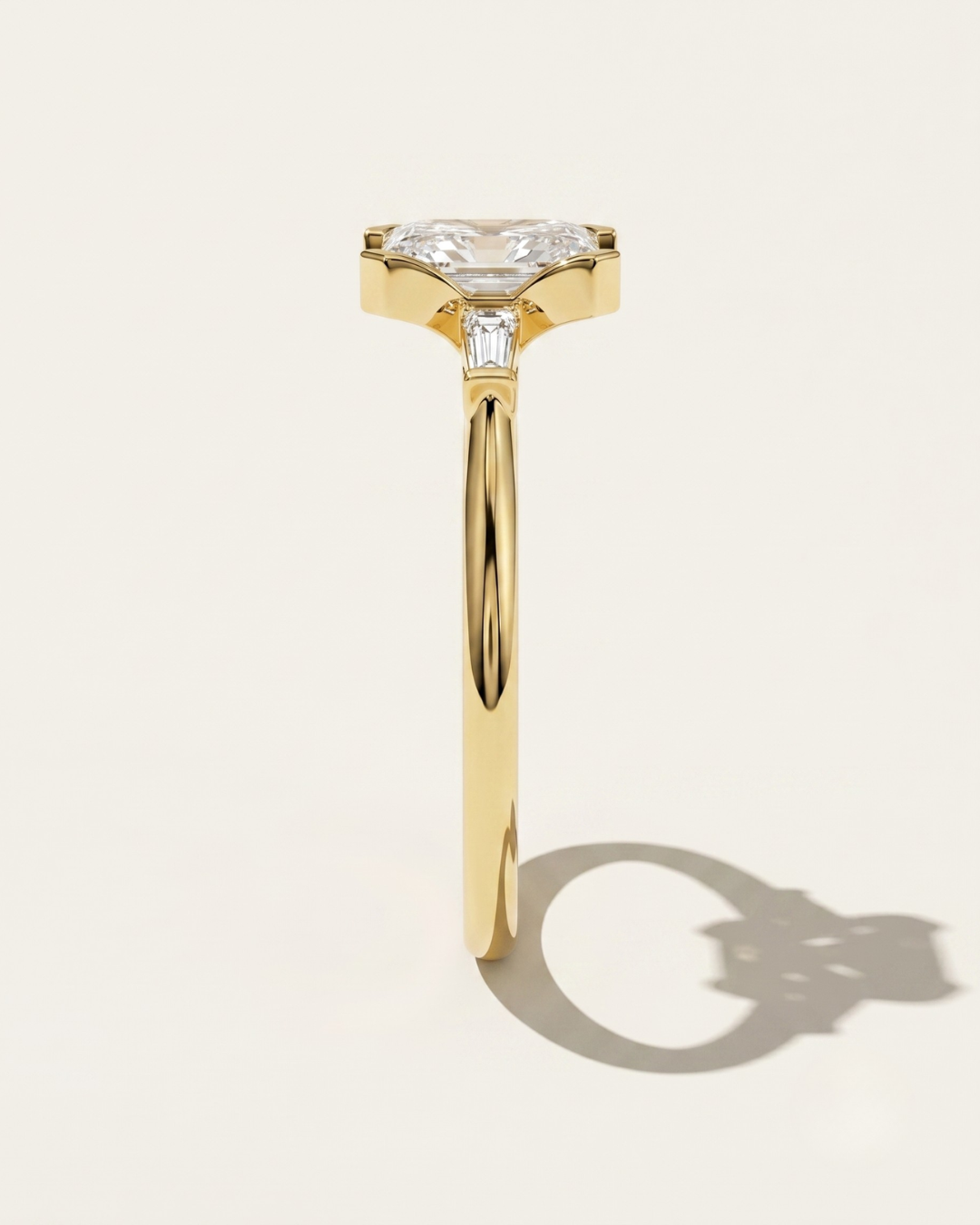 MOHSTEN Montreux 18ct yellow gold three-stone engagement ring back profile with half-bezel emerald cut diamond.