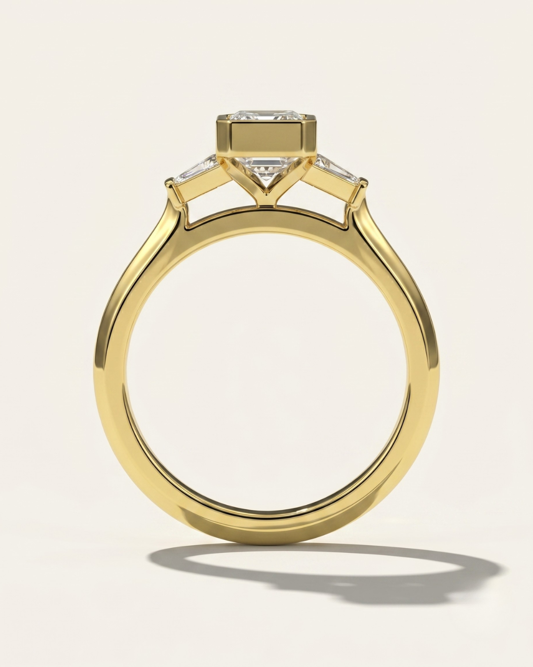 MOHSTEN Montreux 18ct yellow gold three-stone engagement ring standing front view with emerald cut diamond.