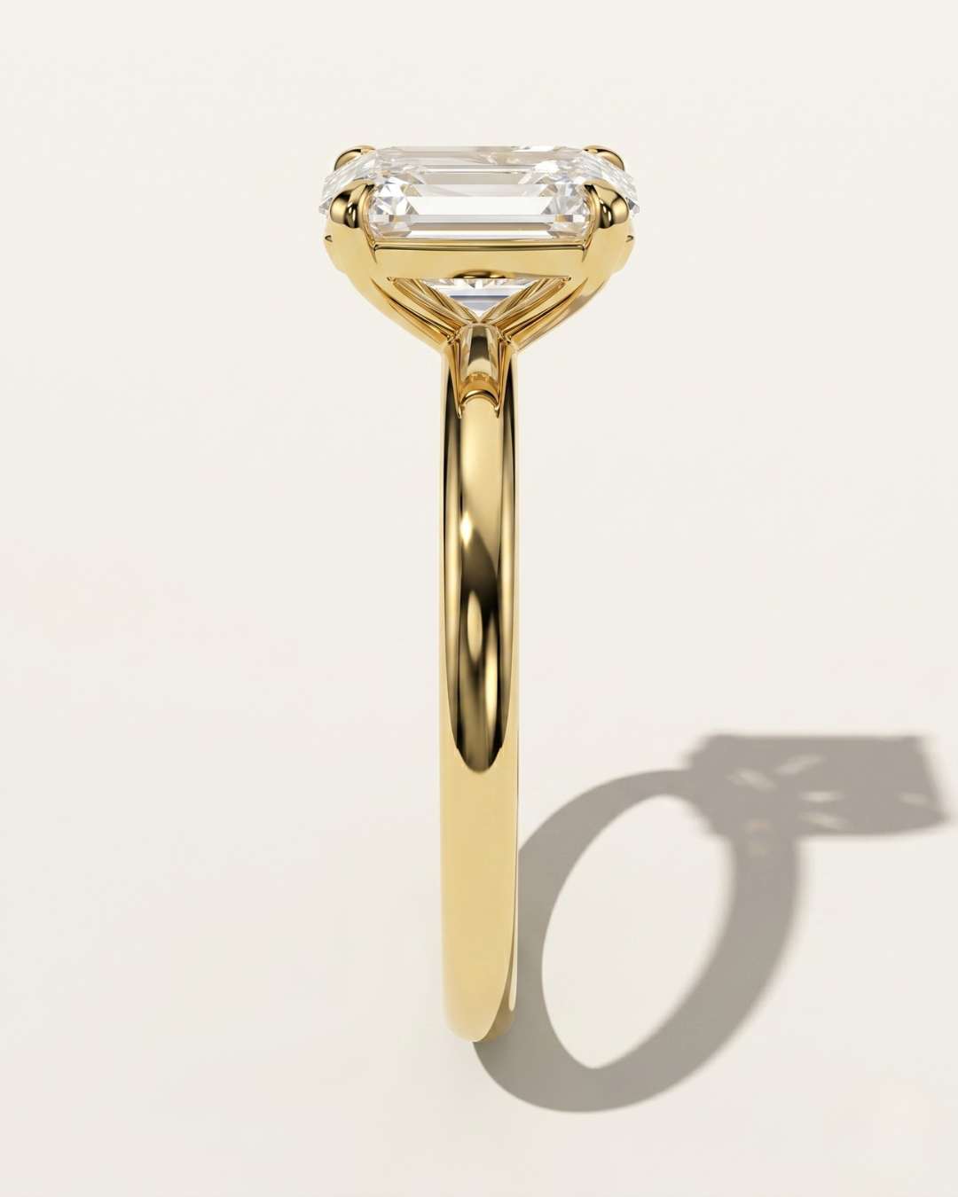 MOHSTEN Osaka oval diamond solitaire engagement ring in 18ct yellow gold, showcasing a crisp side-profile view of the minimalist 4-prong basket setting casting a distinct architectural shadow on a warm studio background.