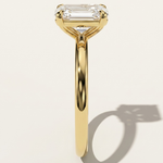 MOHSTEN Osaka oval diamond solitaire engagement ring in 18ct yellow gold, showcasing a crisp side-profile view of the minimalist 4-prong basket setting casting a distinct architectural shadow on a warm studio background.