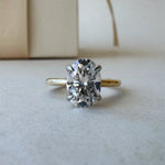 MOHSTEN Osaka oval diamond solitaire engagement ring in 18ct yellow gold showcasing a face-on studio view of the premium oval brilliant centre stone and minimalist 4-prong basket setting resting on a textured surface.